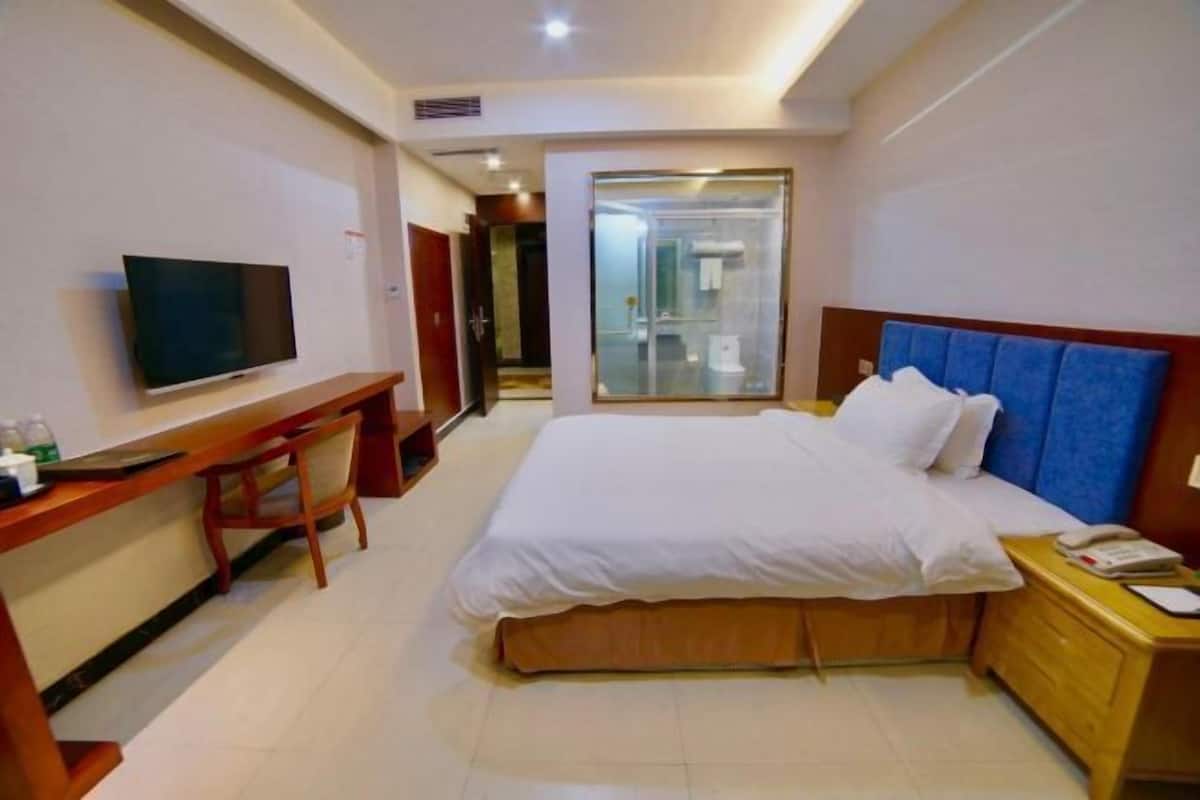 A hotel room with a bed, a desk with a television, a bedside table, and a glass-enclosed shower area.
