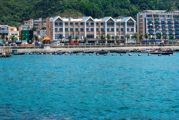 Ein Hotel am Wasser mit mehreren Etagen, einem Steg und Booten sowie einer bewaldeten Hügelsicht im Hintergrund.