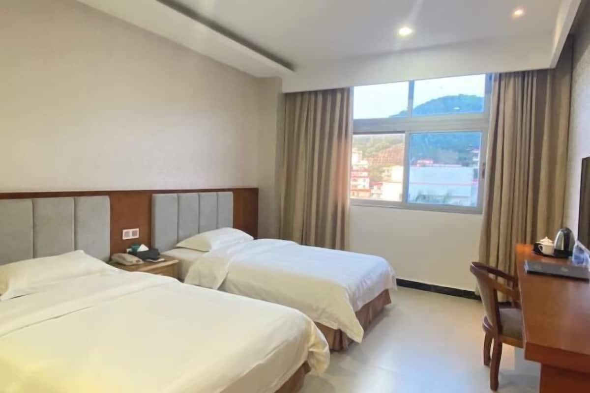 A hotel room with two beds, a desk, and a window with curtains.