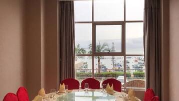 A dining area with a round table, red chairs, and a view of a beach and water through large windows.