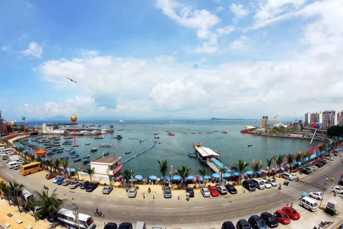 A coastal marina with boats, a parking area, and buildings along the shore.