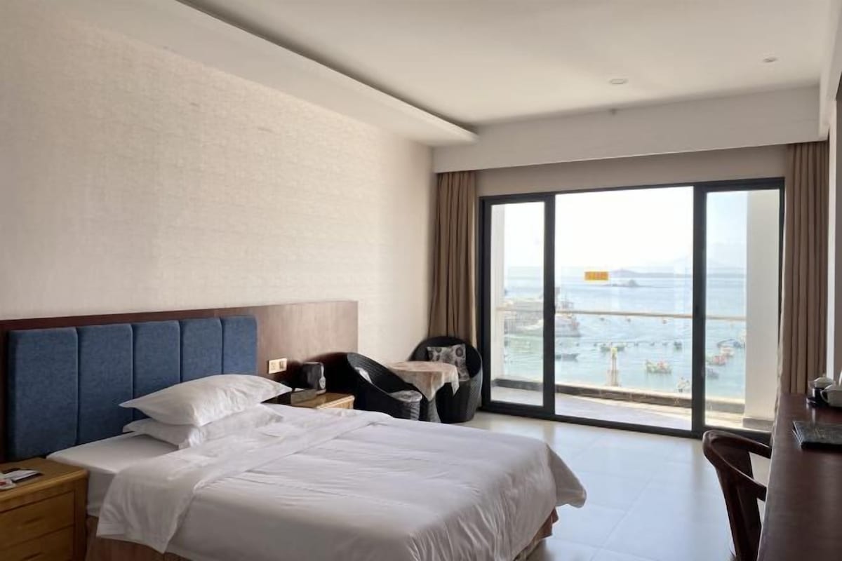 A hotel room with a large bed, a desk, and a view of the sea.