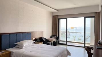 A hotel room with a large bed, a desk, and a view of the sea.
