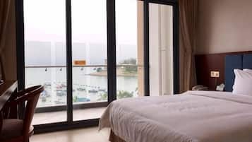 A hotel room with a large window, a bed, a desk, and a chair.