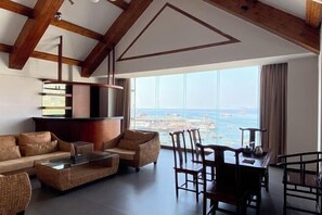 A spacious living area with a high ceiling, wooden beams, a large window with a view of the sea, a sofa, a coffee table, and a dining table with chairs. - Lijing Haiwan Hotel (Shenzhen)