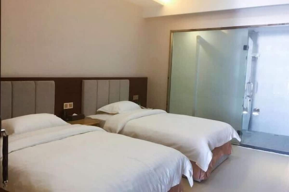 A hotel room with two beds, a sliding glass door, and a bedside table with a lamp.