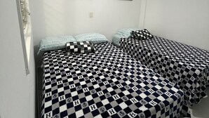 Une chambre avec deux lits, chacun recouvert d’une couvre-lit à carreaux et agrémenté d’oreillers. Deux tableaux sont accrochés au mur au-dessus des lits.