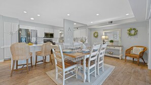 A modern kitchen with white cabinetry, a central island, and a dining area with white chairs and a wooden table. - Family Villa w/ Large Deck&Golf Views, Near Pool/Beach, Bikes (Hilton Head Island)