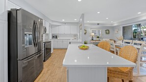 A modern kitchen with white cabinetry, stainless steel appliances, and a central island with wicker chairs. - Family Villa w/ Large Deck&Golf Views, Near Pool/Beach, Bikes (Hilton Head Island)