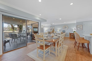 A spacious dining area with a large table and chairs, a kitchen area with white cabinets, and a sliding glass door leading to an outdoor patio. - Family Villa w/ Large Deck&Golf Views, Near Pool/Beach, Bikes (Hilton Head Island)
