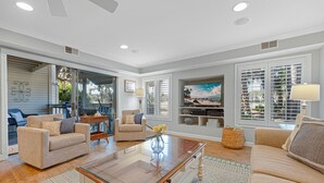 A spacious living room with a glass coffee table, two sofas, a TV, and a large window with blinds. - Family Villa w/ Large Deck&Golf Views, Near Pool/Beach, Bikes (Hilton Head Island)
