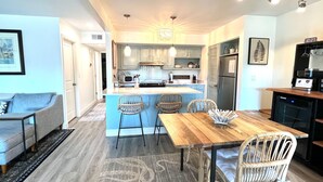 A modern kitchen with a central island, bar stools, and a dining table with chairs. - Courtside Paradise by Sandpiper | Near Beach (Seabrook Island)