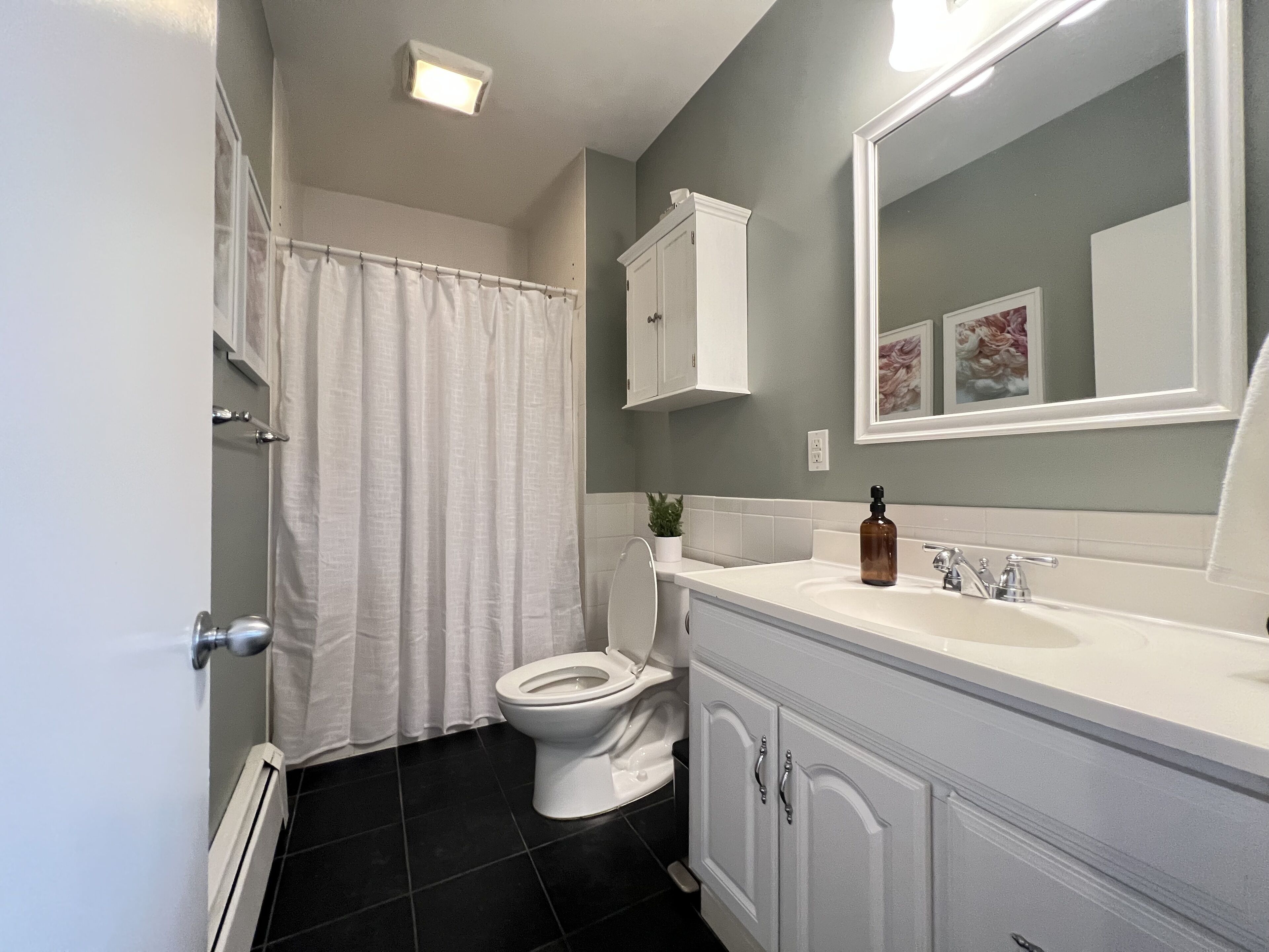 A bathroom with a toilet, a sink, a mirror, and a shower curtain.
