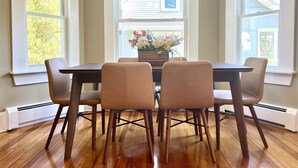 Un comedor con mesa y sillas, una ventana con persianas y vistas a una casa.
