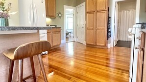 Cocina con armarios de madera, refrigerador blanco, encimera de granito y un taburete de madera.