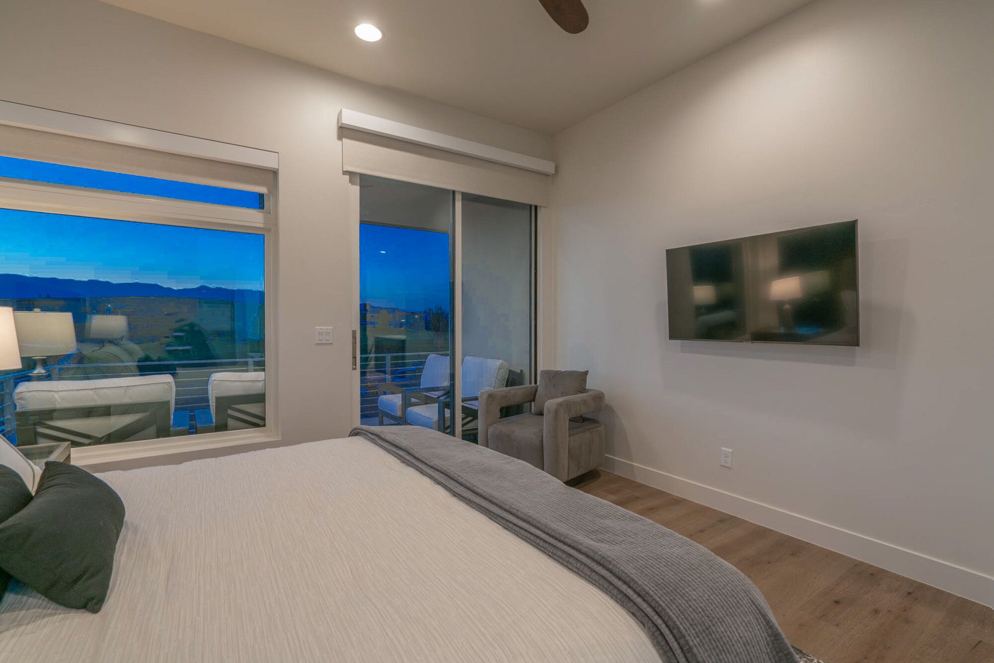 A modern bedroom with a large bed, a TV mounted on the wall, and a balcony with a view.