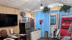 Una habitación compacta con cama, kitchenette, televisión y ventilador.