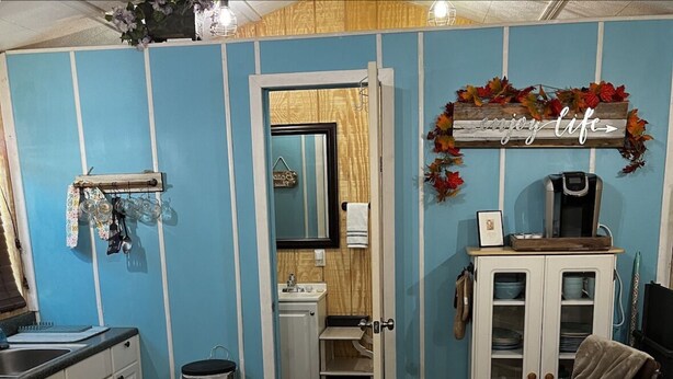 Una cocina compacta con un lavamanos, armarios y una cafetera. Hay una pequeña zona de comedor con una silla y una mesa.