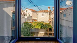 Vista desde una ventana que da a una calle estrecha con edificios, un muro de piedra y un pequeño jardín.