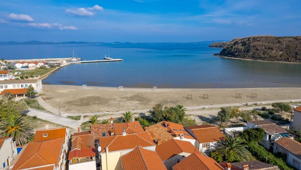 Un pueblo costero con edificios de tejados terracota, una playa de arena y un mar tranquilo.