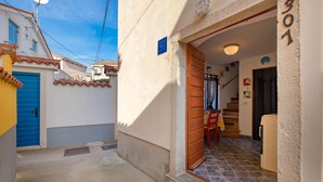 Una calle estrecha con una puerta azul, una escalera que sube al segundo piso y un suelo de baldosas.