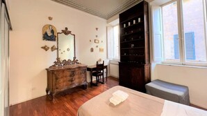 Een slaapkamer met een houten dressoir, een bed met een witte dekbedovertrek, een grote spiegel en een boekenkast.