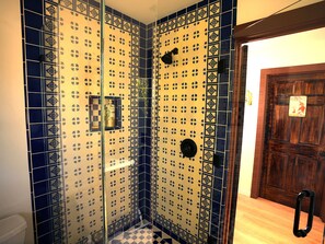 A bathroom with blue and yellow patterned tiles, a shower area, and a wooden door.
