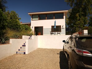 A modern two-story house with a patio, a car parked in front, and a staircase with blue tiles.