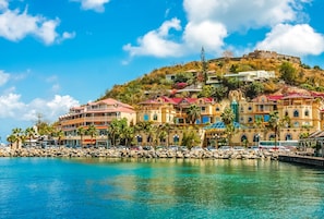 A coastal hotel with multiple buildings, a rocky shoreline, and a hill with a fort.