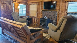 Un interior de cabaña acogedor con chimenea de piedra, muebles de madera y un televisor de pantalla plana montado encima.