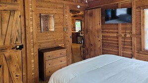 Un dormitorio tipo cabaña de madera con una cama, un tocador, un televisor y un ventilador de techo.