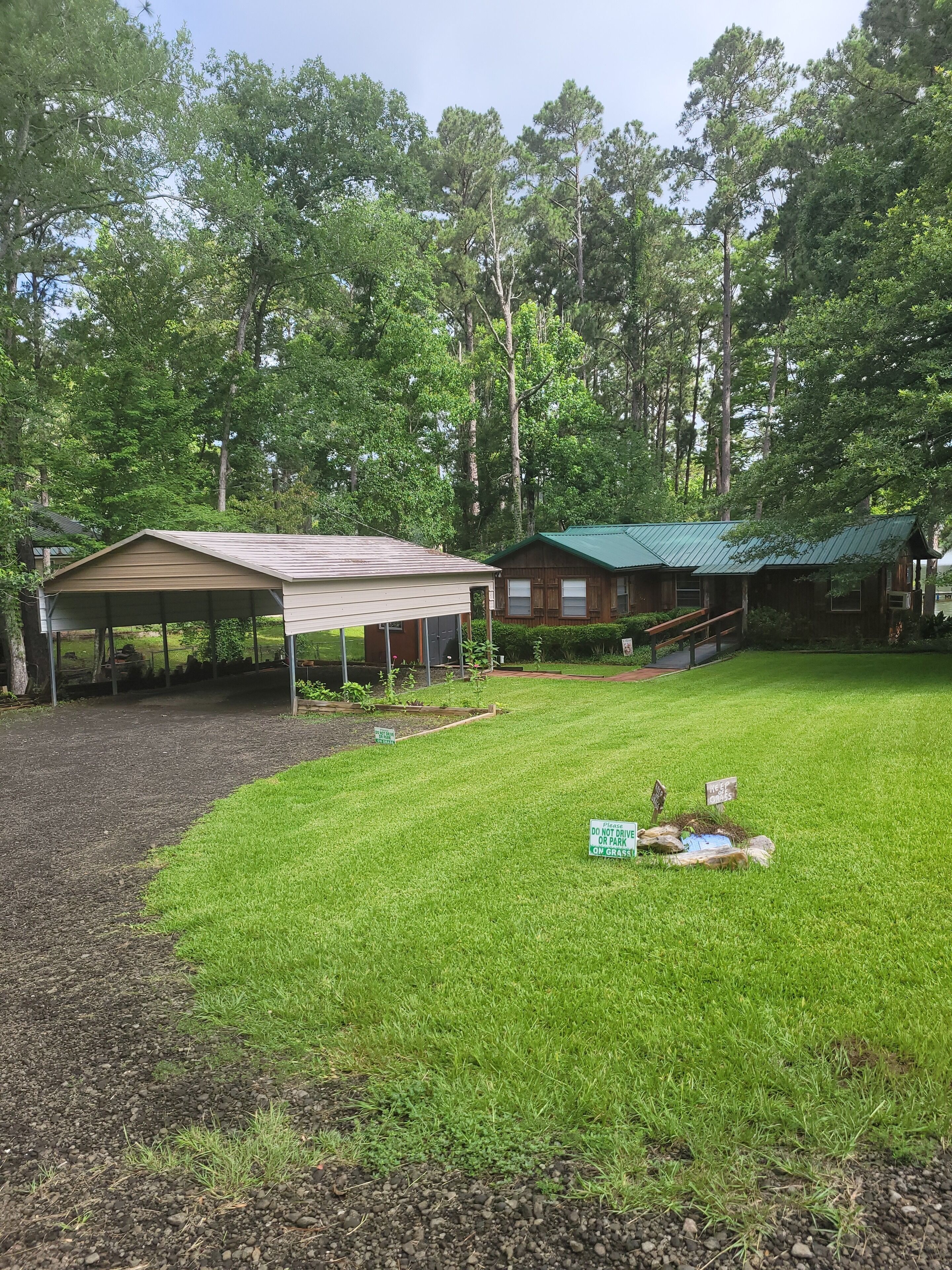 A covered outdoor area with a wooden cabin and a green-roofed building, surrounded by dense trees.