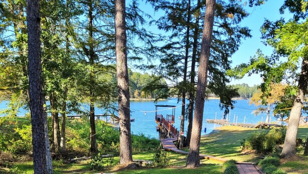 Una terraza de madera con dos sillas Adirondack rojas y una mesa de picnic, con vistas a un lago que tiene un muelle y un pabellón.
