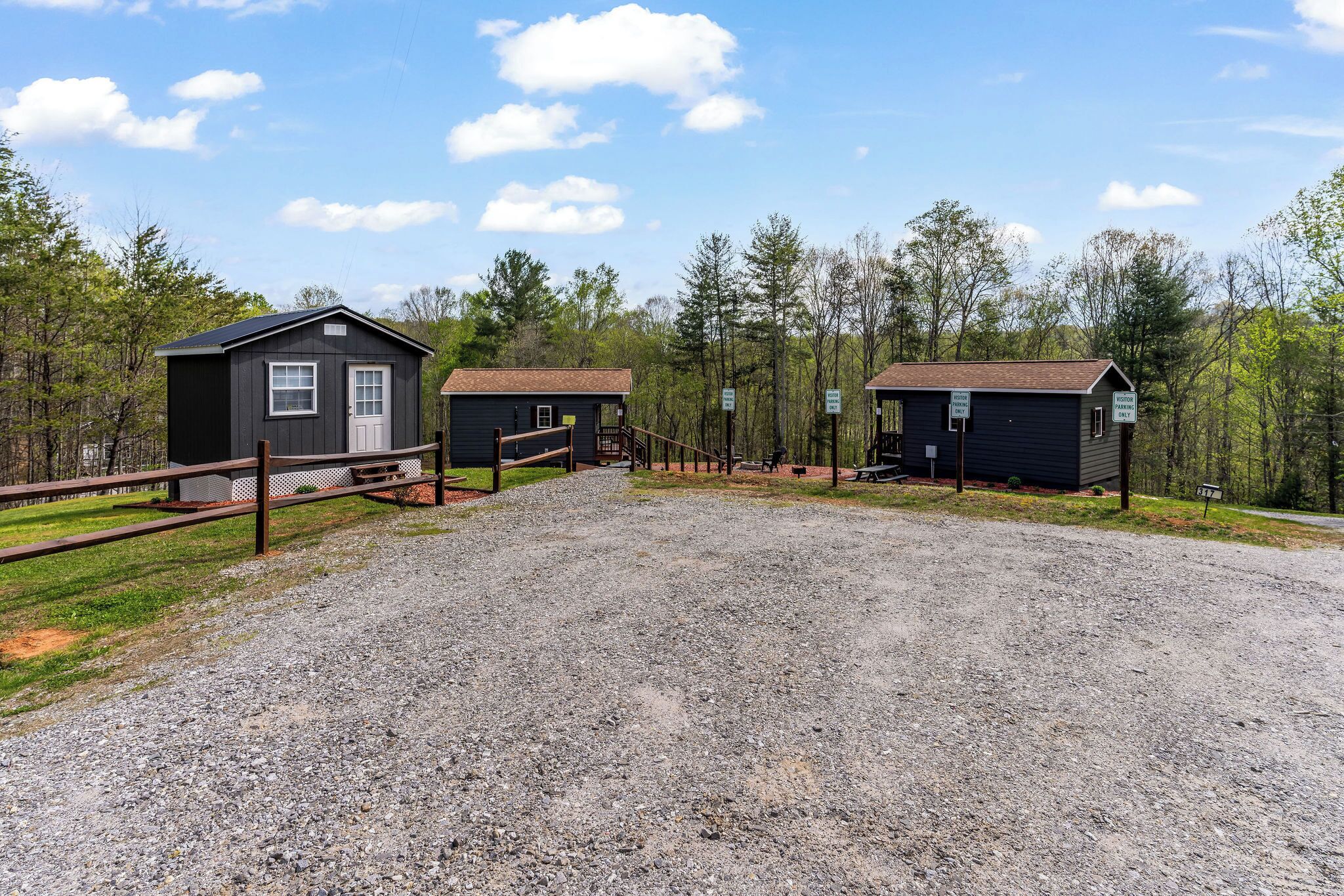 A gravel driveway leading to two small cabins with wooden fences and picnic tables.