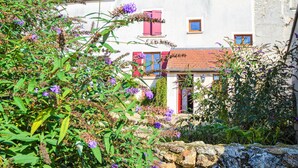 Ein traditionelles europäisches Gebäude mit Steinwand, roten Fensterläden und einem Garten mit violetten Blumen.