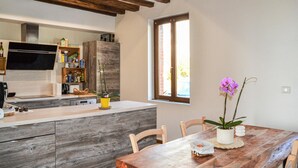 Eine Küche mit Holzausstattung, einem eingebauten Backofen und einem Fenster. Ein Esstisch mit Stühlen und eine Topforchidee sind ebenfalls vorhanden.