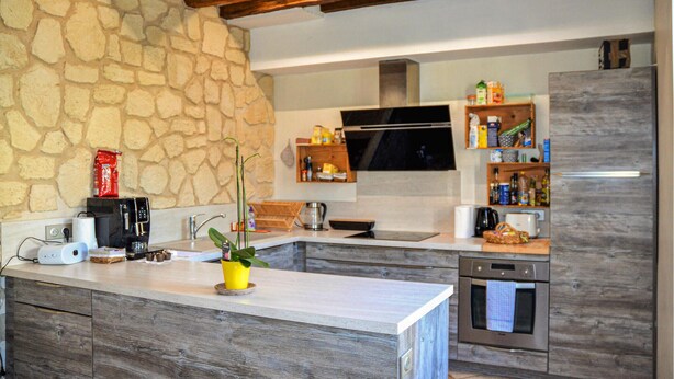 Eine moderne Küche mit Steinwand, Holzbalken, einem eingebauten Backofen und verschiedenen Geräten sowie Stauraumschränken.