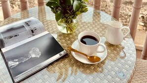 A glass table with a book, a cup of coffee, a white mug, and a potted plant on a balcony overlooking the beach. - Moet Cartagena Hotel Boutique  - Adults Only (Cartagena)