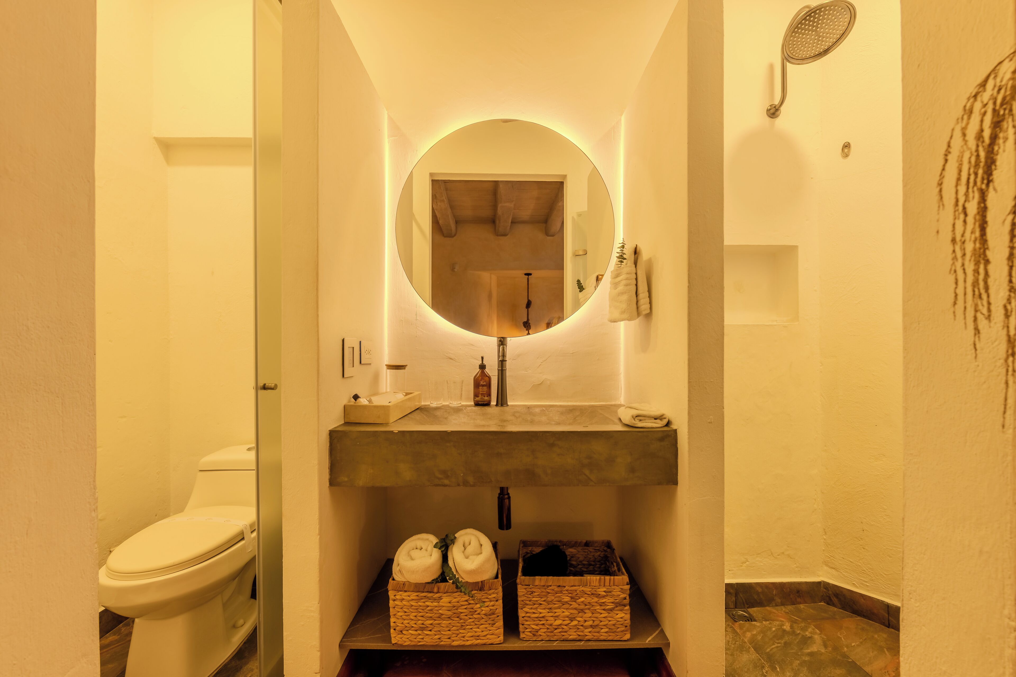 Un baño con un espejo redondo, inodoro, lavabo y ducha.