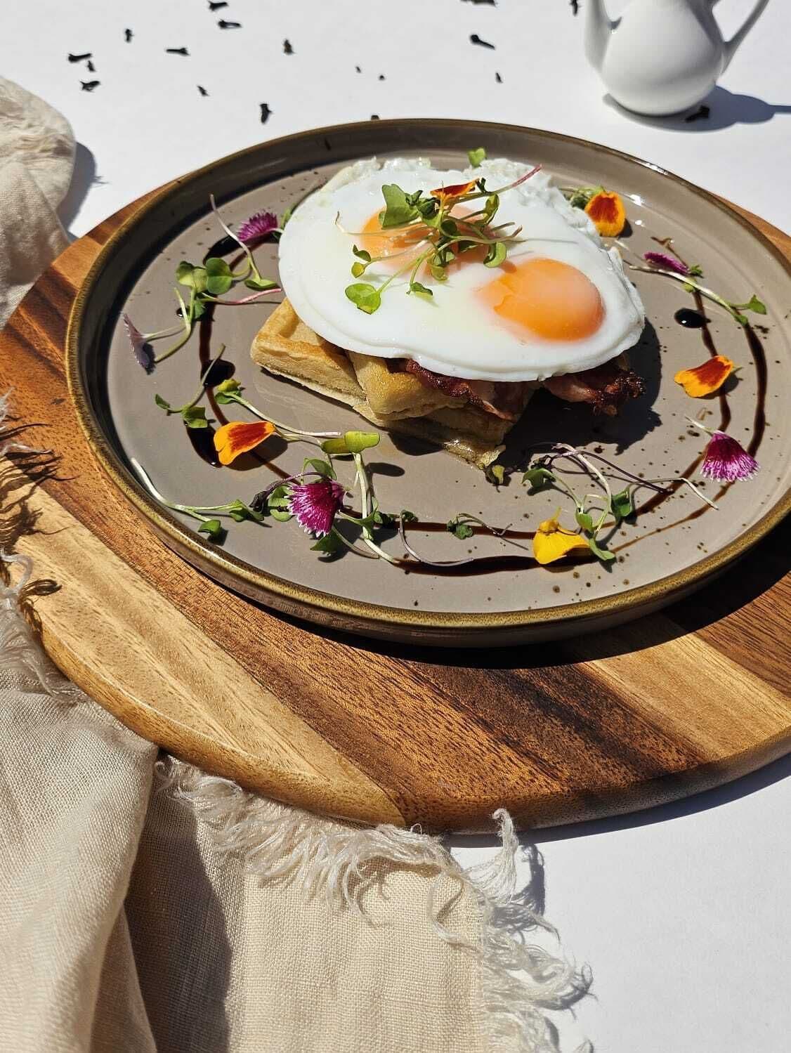 Un plato de comida con un huevo escalfado, tocino y verduras, sobre una tabla de madera.