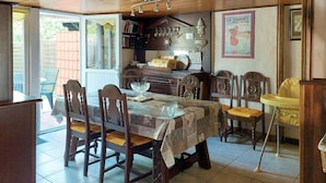 Un coin repas avec une table dressée pour quatre personnes, entourée de chaises en bois. On y trouve une bibliothèque remplie de divers objets, une chaise haute pour bébé et une affiche accrochée au mur.