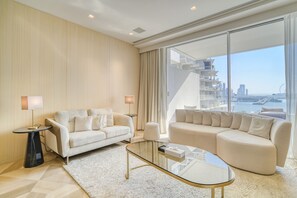 Un salon moderne avec un canapé, une table basse en verre et une vue sur le paysage urbain, visible à travers de grandes fenêtres.