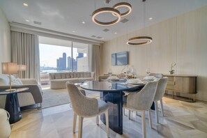 Et moderne hotelværelse med spiseplads, der inkluderer et glasbord, stole, en sofa og udsigt over byen.