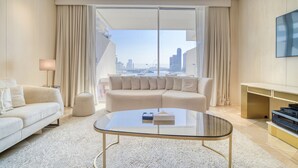 Una habitació d'hotel moderna amb una finestra gran que ofereix una vista a la ciutat, una taula de cafè de vidre, un sofà beix i una televisió de pantalla plana penjada a la paret.