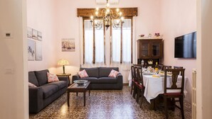 A living room with a sofa, coffee table, dining table, chandelier, and artwork on the walls. - Villa Perondi by MMega (Camaiore)