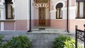 A building entrance with a wooden door, a small step leading up, and a metal gate. - Villa Perondi by MMega (Camaiore)