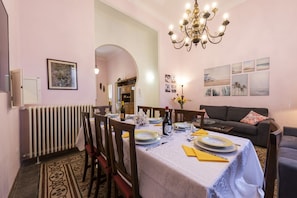 A dining area with a table set for four, a chandelier, and a sofa in the background.