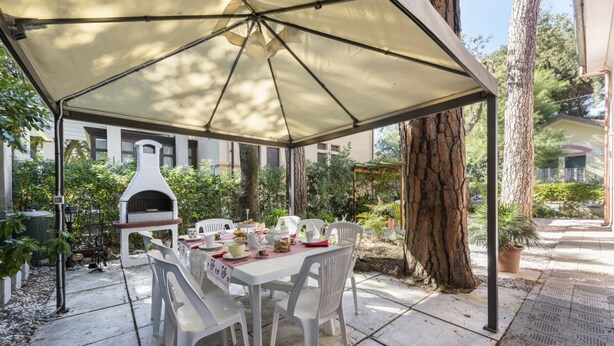 A covered patio with a table and chairs, a pizza oven, and a pergola structure. - Villa Perondi by MMega (Camaiore)