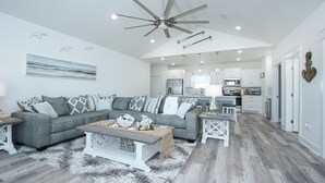 A spacious living room with a grey sectional sofa, a coffee table, and a ceiling fan. - S.S. Esmeralda-Newly built home-3min from beach (Bolivar Peninsula)