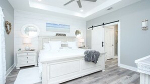 A bedroom with a large bed, two bedside tables, a ceiling fan, a sliding door, and a framed picture on the wall. - S.S. Esmeralda-Newly built home-3min from beach (Bolivar Peninsula)